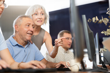 Fototapeta premium Elderly people help each other learn how to use computer. Woman suggests right decision to an mature man