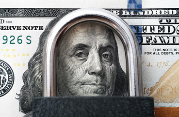 Close-up of a U.S. one-hundred-dollar bill, with Benjamin Franklin’s face under metal padlock....