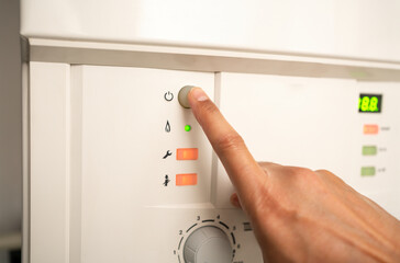 Cropped view of a man's hand pushing a button on the boiler of heating and hot water