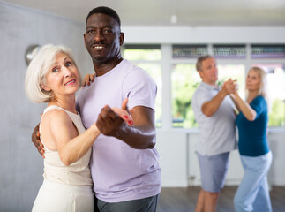 Group of positive adults doing Tango poses in training room during workout session