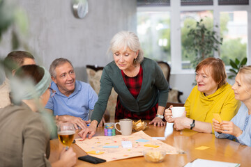 Fototapeta premium Retirees play board games and drink tea with cookies