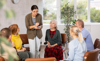 Friendly young girl conducting language speaking club, communicating with group of interested older...