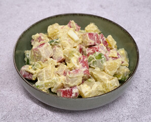 Seafood salad. Closeup view of a fresh salad with boiled sliced potatoes, chopped hard boiled egg, avocado, crab sticks and mayonnaise in a bowl on the white table