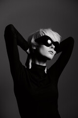 Stylish woman with short hair in black attire, wearing large sunglasses, posing gracefully against...