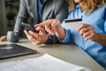 close up of two colleagues buy online on mobile phone with credit card