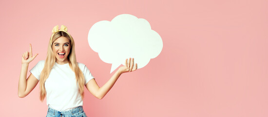 Amazing Offer. Overjoyed blonde girl holding empty speech bubble, pointing finger up, pink studio wall, copyspace