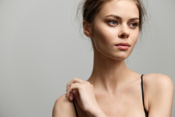 Naklejka premium Elegant young woman with natural makeup, gazing thoughtfully, dressed in a simple black top. Soft gray background emphasizes her serene expression and beauty.
