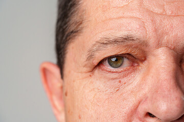 Vew of an older man's face highlighting expressive eyes and textured skin with soft lighting in a neutral setting