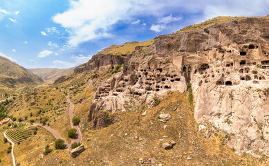 Fototapeta premium Aerial top view of Vardzia city on sunny summer day. Ancient cave monastery in Erusheti Mountain rocks at Kura River. Monument of medieval Georgian architecture, carved in rough rock. Georgia, Europe.