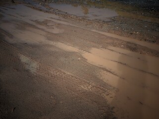 Muddy dirt road with tire tracks and puddles.