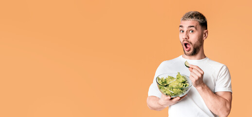 Healthy eating concept. Surprised guy with open mouth eating salad, free space