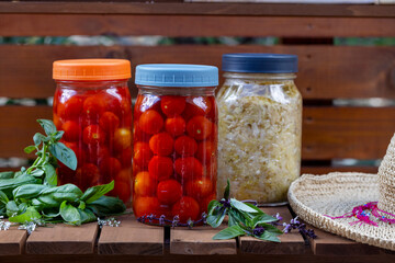 Fermentation of cherry tomatoes and cabbage on a wood garden cart with basil leaves and straw hat