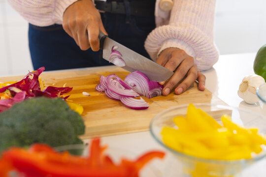 Asian woman chopping red onion on cutting board with colorful vegetables in kitchen, at home