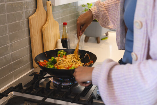 Cooking stir-fry noodles with vegetables on stove in cozy kitchen, at home