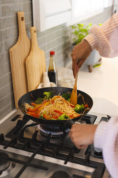 Cooking stir-fry noodles with vegetables on stove in modern kitchen, at home