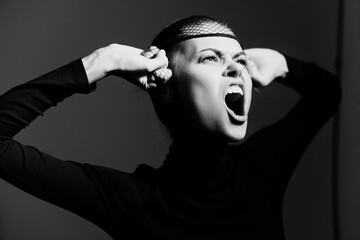 Expressive woman in black attire demonstrating frustration with hands on head, showcasing powerful emotions against a dark background.