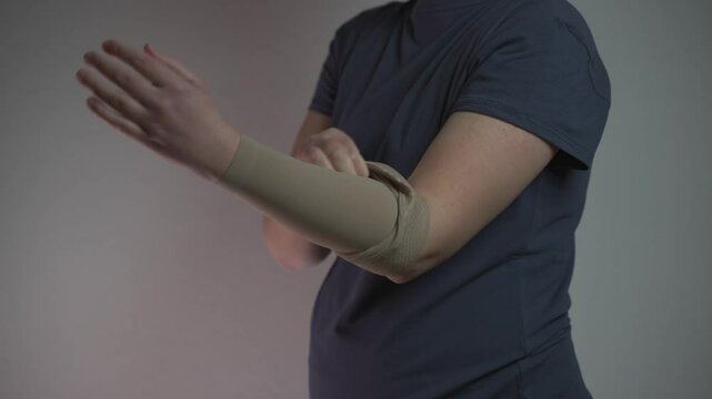 Prophylactics of thrombosis. Woman removes compression sleeve from left hand on gray background. Effective anti-thrombosis therapy involves compression sleeves to improve vein health and blood flow. 
