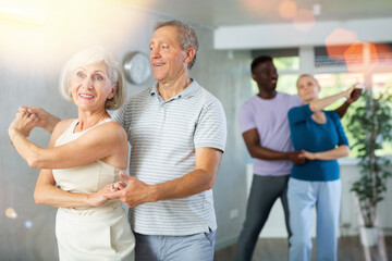 Obraz premium Group of positive adults doing Tango poses in training room during workout session