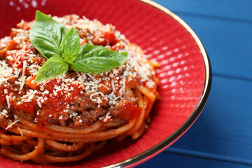Delicious pasta bolognese with basil on blue wooden table, closeup