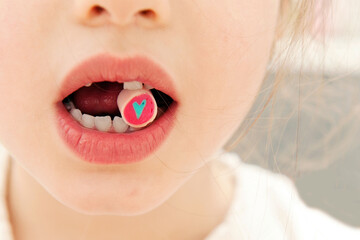 Fototapeta premium A close-up of a child's mouth holding a colorful candy with a heart design 