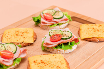 Light Breakfast. Quick and Healthy Sandwiches. Rice Cakes with Ham, Tomato, Fresh Cucumber, Green Salad and Cheese on Wooden Cutting Board. Beige Background