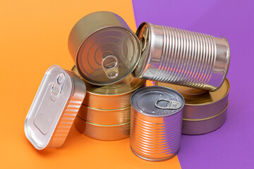 A Group of Stacked Tin Cans with Blank Edges on Split Orange and Violet Background. Canned Food. Different Aluminum Cans for Safe and Long Term Storage of Food. Steel Sealed Food Storage Containers