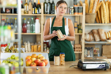 Portrait of a friendly girl seller behind a store counter offering to buy canned beans and legumes