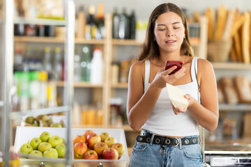 Young female shopper scanning qr code for packaged cheese in grocery store