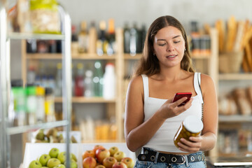 Young female shopper scanning qr code for olives in jar in grocery store