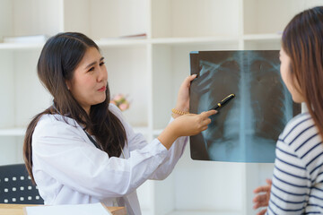 Asian female doctor explaining lung x-ray film of a female patient at the hospital.