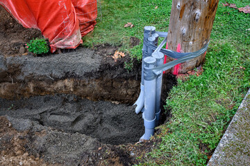PVC pipes temporarily duct taped to a wood utility pole to hold them in place, pipe conduits running in a dug-out trench backfilled with gravel
