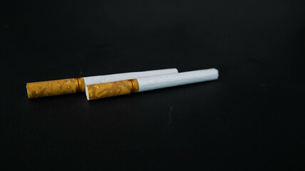 Two cigarettes placed on a black surface, highlighting the contrast between the white paper and the dark background. Ideal for themes related to smoking, health, or lifestyle.