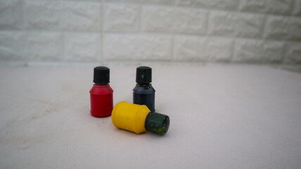 Three small paint bottles in black, yellow, and red colors on a white surface with a blurred brick wall background. Perfect for art and craft themes.