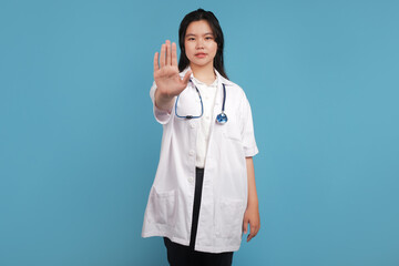 doctor holding a stethoscope. Angry young Asian woman doctor wearing uniform with a stethoscope frowning displeased, extend hand to show stopping, disagree, prohibit or forbid on blue background. Heal