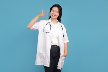 Smiling professional doctor in medical uniform shows thumbs up. Pleased asian female physician confirms smth, recommending product, isolated on blue. Potrait female doctor with stethoscope