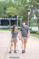 A Chinese-Malaysian couple in their 30s walk together in a green park with abundant water in Kuala Lumpur, Malaysia, on a sunny day in June 2024.