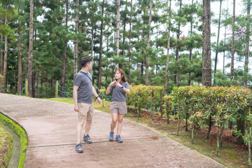 Obraz premium A Chinese-Malaysian couple in their 30s walk together in a green park with abundant water in Kuala Lumpur, Malaysia, on a sunny day in June 2024.