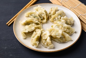 Steamed dumpling filled with pork and vegetables on dish and chopsticks on black background