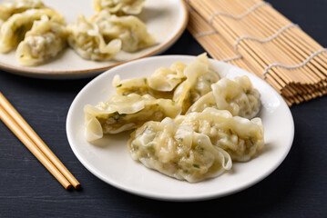 Steamed dumpling filled with pork and vegetables on dish and chopsticks on black background