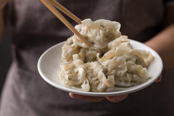 Hand holding chopsticks and eating steamed dumpling filled with pork and vegetables on dish