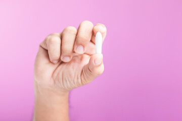 A hand holding a suppository for hemorrhoid treatment, symbolizing proactive health care and self-care. Set against a soft pink background, emphasizing the importance of managing health needs