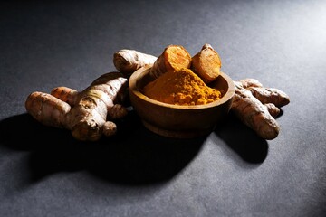 Fresh turmeric root and turmeric powder in a wooden bowl, turmeric isolated on dark background, spice concept