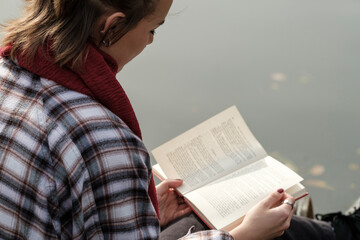 Young woman reading a book by the water