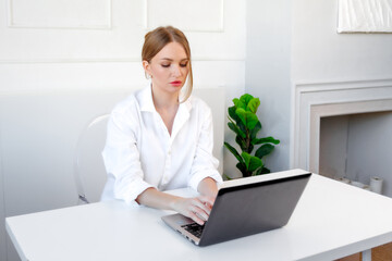 A focused young woman working on her laptop at a minimalistic desk in a bright and airy office space during the afternoon