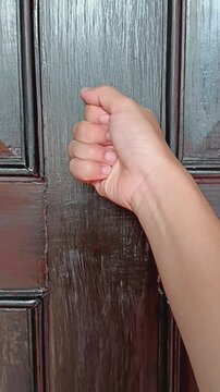 Woman hands knocking with back of fist on wooden door.