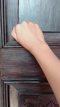 Close up of Woman's hand knocking fist on wooden door.