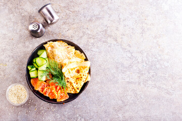 Thin pancakes or crepes with smoked salmon, cucumber and dill on a gray background.