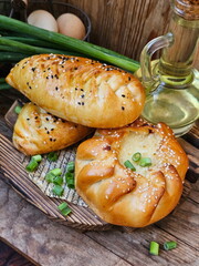 Pies with green onions and egg on a wooden background