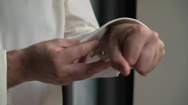 A detailed closeup of a hand skillfully fastening a cufflink on a pristine white formal shirt, showcasing elegance