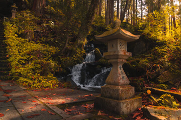 夕日を浴びて静かに立つ石灯篭と沢のせせらぎ